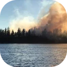 A fire as seen from across a lake - its smoke cloud turning black.