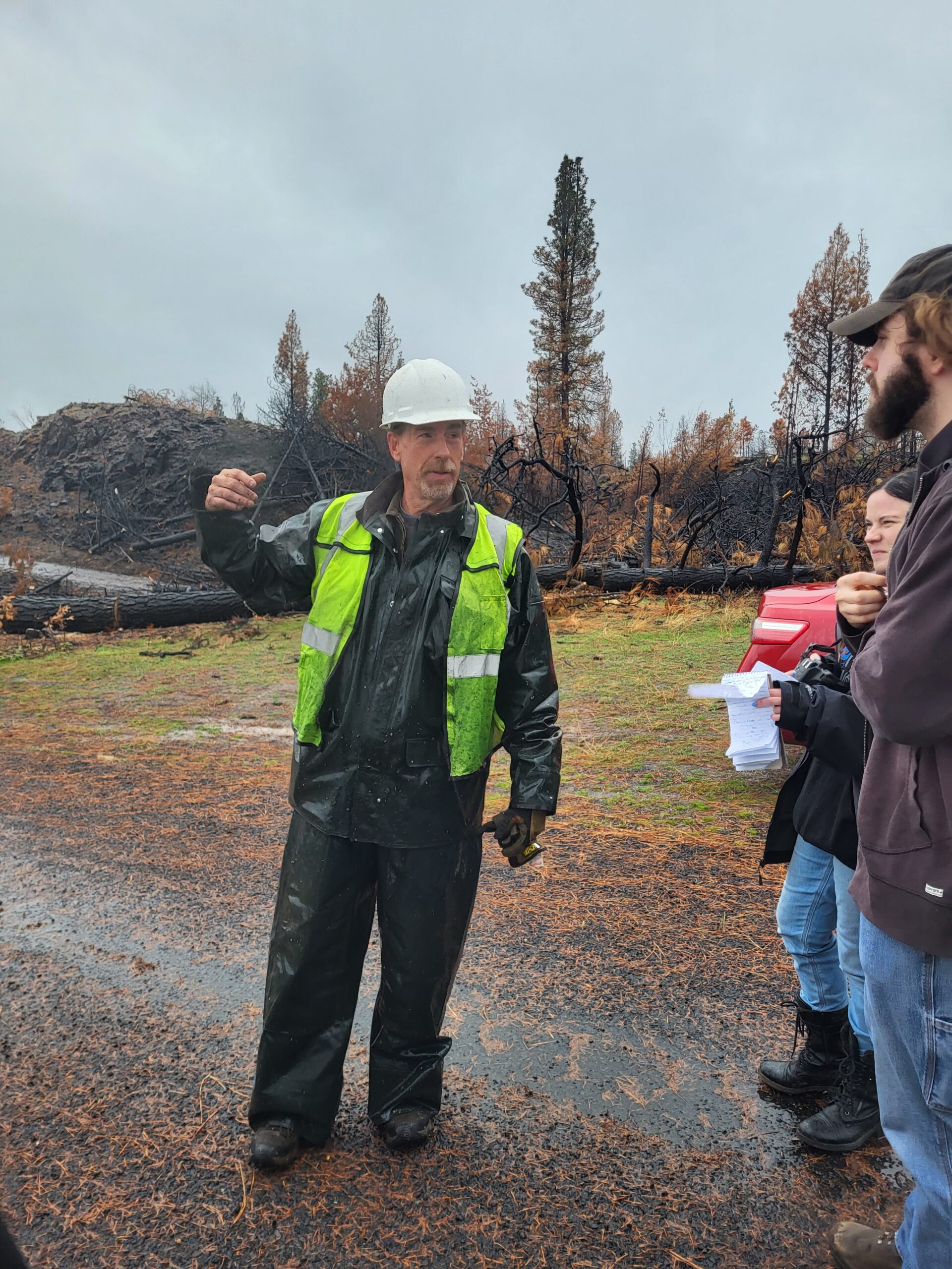A traffic volunteer talking with other volunteers about the damage caused by the fire, gesturing to the debris.